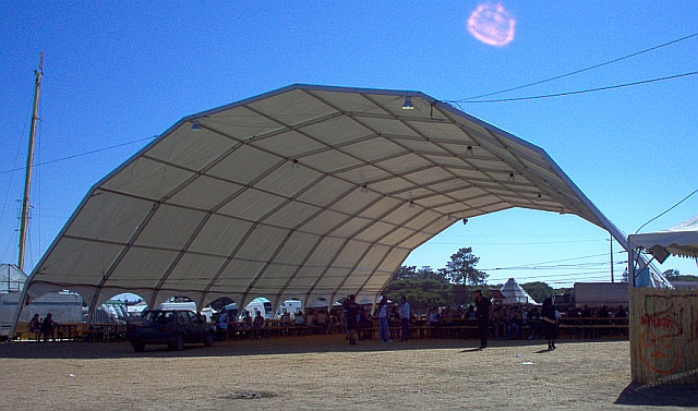 A large open tent-like structure with tables full of people beneath